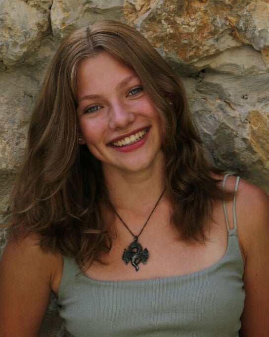 a woman with short curly hair wearing a necklace leaning on the stone wall
